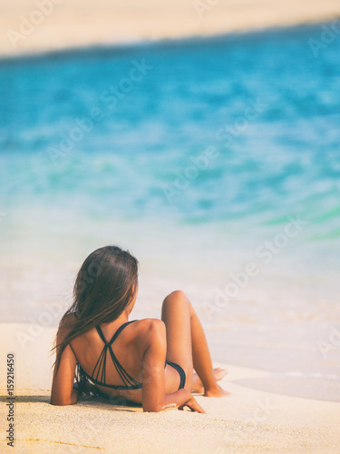 Beach vacation relaxing young girl lying down on sand sunbathing at tropical holiday destination.
