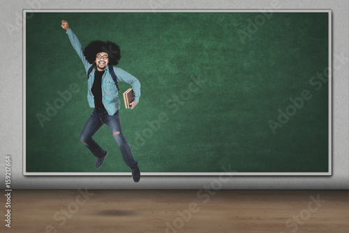 Afro man jumping with book in classroom © Creativa Images