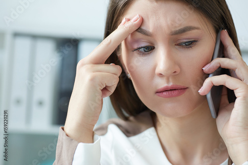 Stressed businesswoman talking on phone while working on computer at desk in office.