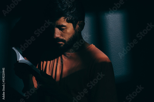 Foto Prisoner man in dark cell reading a book or bible