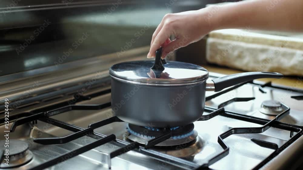 Static shot female petite hand checking on a pan with boiling water, which stands on stainless steel pristine perfectly clean range stove that works on natural gas Static shot female petite hand checking on a pan with boiling water, which stands on stainless steel pristine perfectly clean range stove that works on natural gas