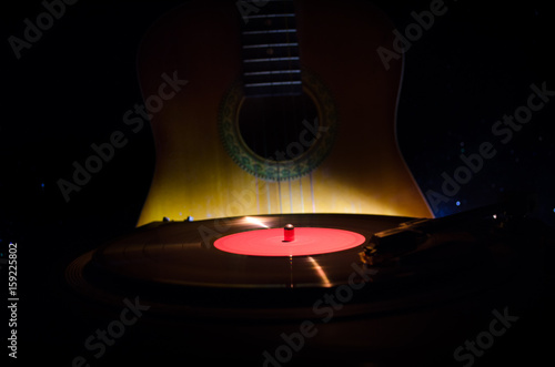 Vintage vinyl record playing on player and acoustic guitar on background with fire orange smoke. Blues concept.