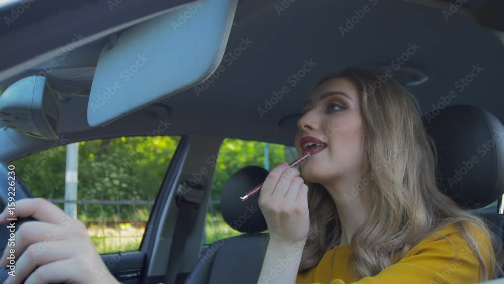 Girl paints her lips while sitting behind the wheel of a car Girl paints her lips while sitting behind the wheel of a car