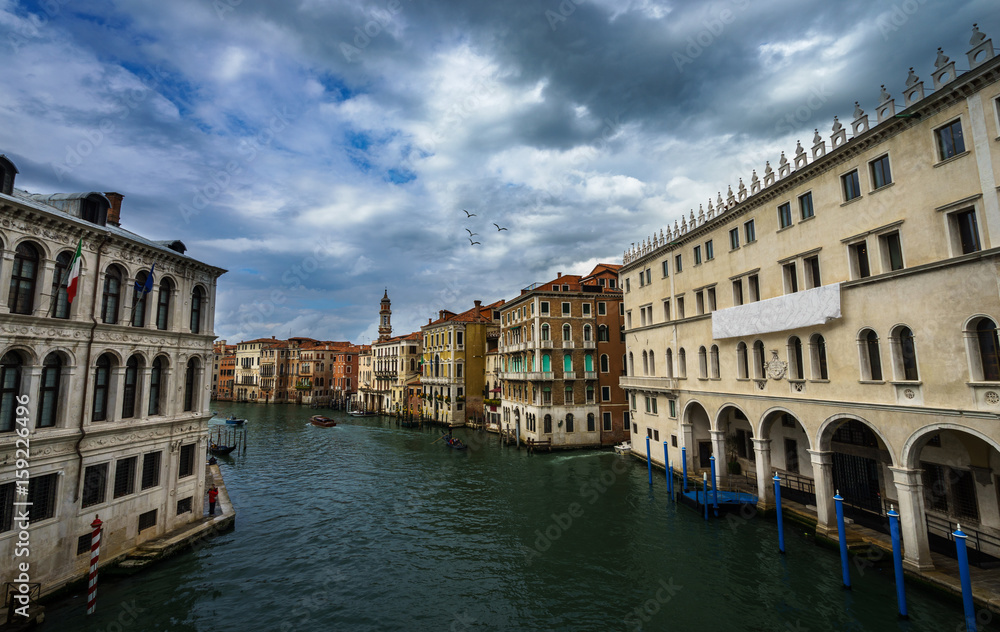 Panoramic view on famous Grand Canal among historic houses in Venice, Italy at dark, cloudy day with dramatic sky.