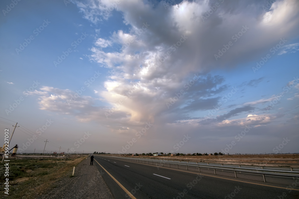 Road vanishing to the horizon under sun rays coming down trough the dramatic stormy clouds. Sunset at the mountain road. Azerbaijan, Ganja