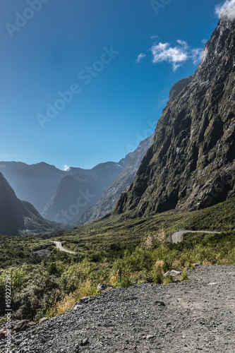 Fiordland National Park, New Zealand - March 16, 2017: Mountain range and road down under Hommer Tunnel under blue sky. Sparse green non-tree vegetation. photo