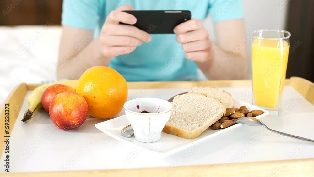 Young man having breakfast in bed and texting messages on smartphone, steadycam shot
Young man having breakfast in bed and texting messages on smartphone, steadycam shot