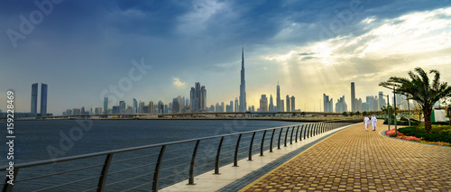 Panoramic view of business bay, downtown area of Dubai and two arab men take a walk on the promenade at cloudy day. UAE photo