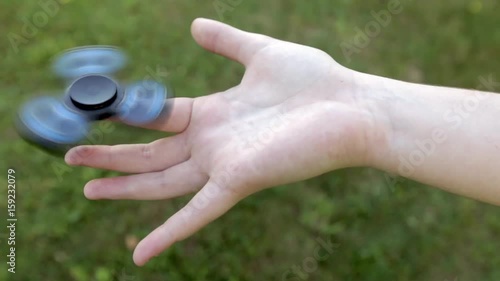 Girl's hand holding a spinning fidget spinner in her hand, spinning them on her index finger; against the green grass background