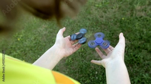 Girl's hand holding a spinning fidget spinner in her hand, spinning them on her index finger; against the green grass background