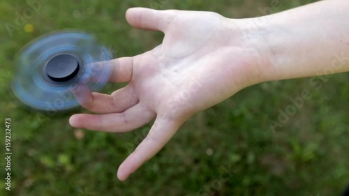 Girl's hand holding a spinning fidget spinner in her hand, spinning them on her index finger; against the green grass background