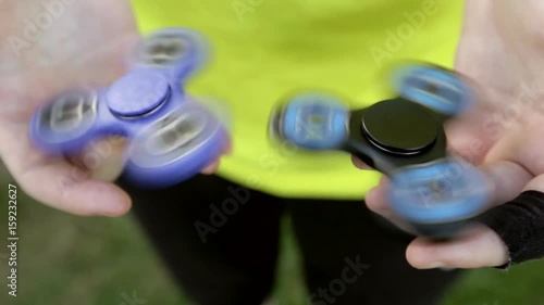 Girl holding blue and black fidget spinners in her hands, view from above; both gadgets spinning 