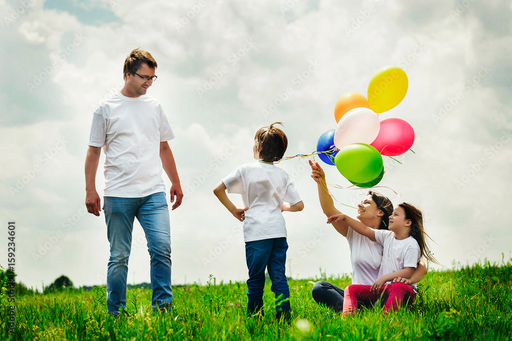 happy family sitting with balloons outdoor on a warm summer day.