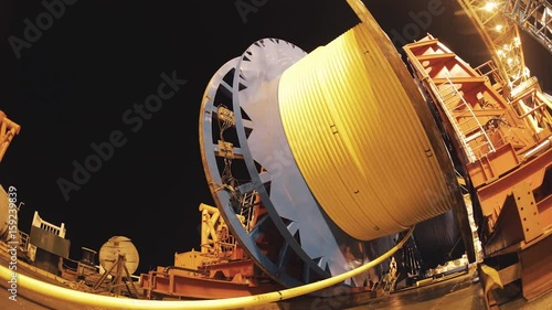 Timelapse massive metal blue wheel roll and unroll long yellow hose on water oil production platform, day night change