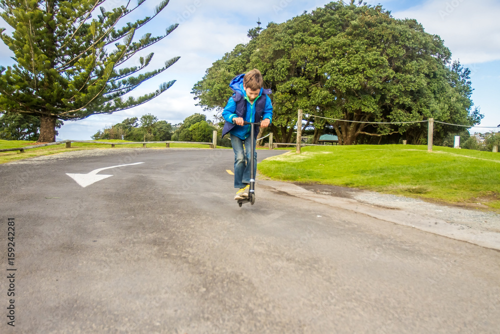 outdoor portrait of young happy preteen boy riding a scooter on natural background