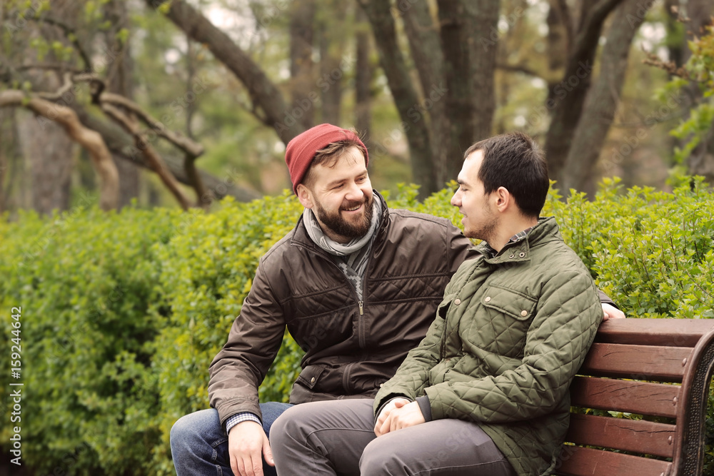 Happy gay couple sitting on bench in park Happy gay couple sitting on bench in park