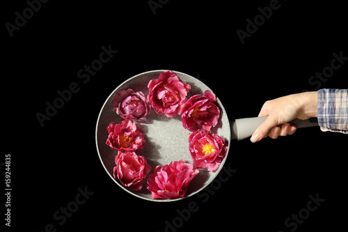 Female hand holding composition of frying pan and tulips on black background