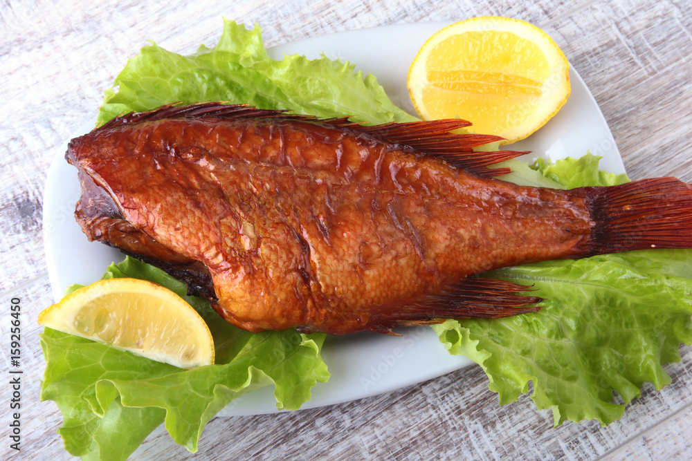 Smoked fish and lemon on green lettuce leaves on Wooden cutting board isolated on white background. Smoked fish and lemon on green lettuce leaves on Wooden cutting board isolated on white background.