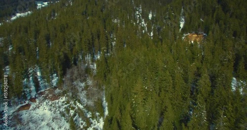 Luftaufnahme in verschneitem Bergwald mit Kamerafahrt zu Höhle im felsigen Berg
