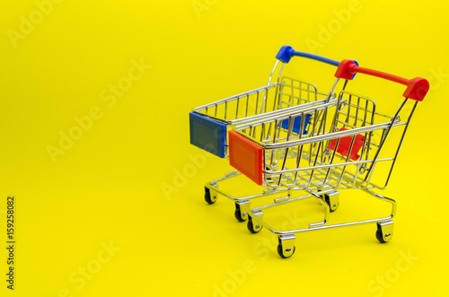 mini supermarket shopping cart blue and red color on yellow background, holiday sale and online shopping concept, selective focus, copy space