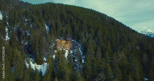 Luftaufnahme in verschneitem Bergwald mit Kamerafahrt zu Höhle im felsigen Berg, nah