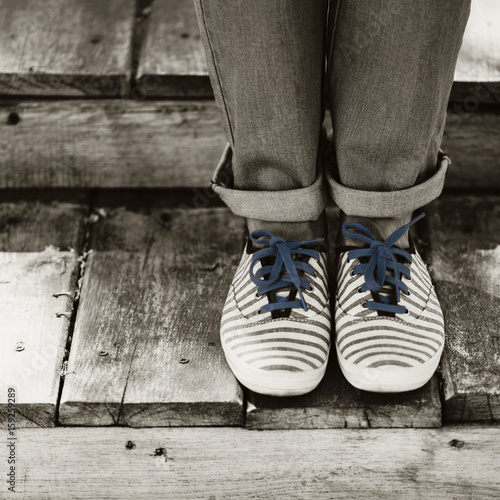 Black and white photography. Female legs in jeans and striped sneakers on old wooden steps.
