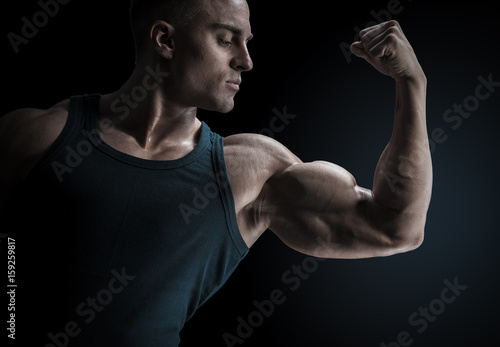 Young confindent muscular bodybuilder guy standing on black background and posing biceps muscle Classic bodybuilding © USM Photography
