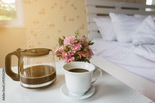 Black coffee is placed on the table in the bedroom with morning light.