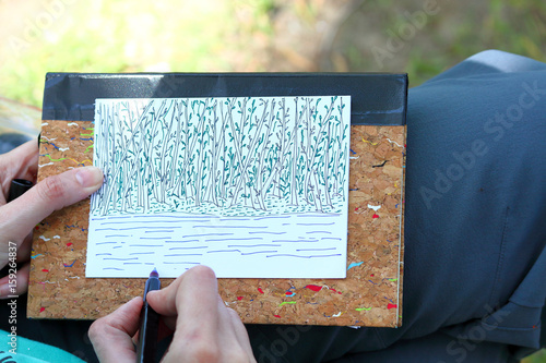 Hand of girl drawing an abstractionary fantastic sketching card with trees and grass in doodling style photo