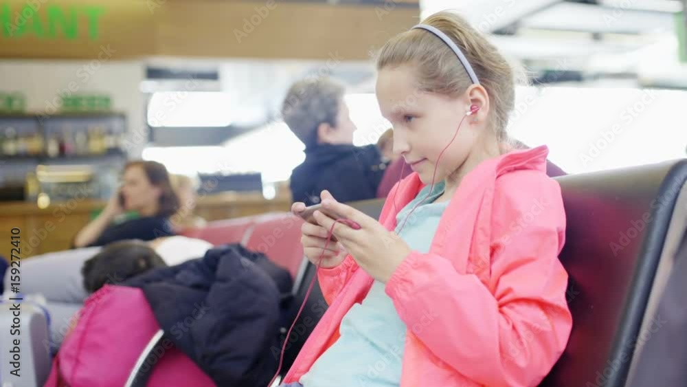Little girl playing games on smartphone in airport departure area Little girl playing games on smartphone in airport departure area