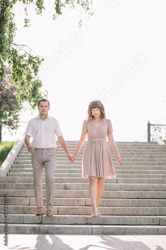 beautiful couple on a walk, the girl in the beige dress and the guy wearing light clothing go up the stairs, down, happy, holding hands, Park, summer, nature photo