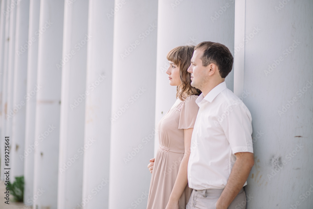 a love story, a man and a woman wearing light clothes, standing near a grey wall, profile, hug, family, a date, a walk