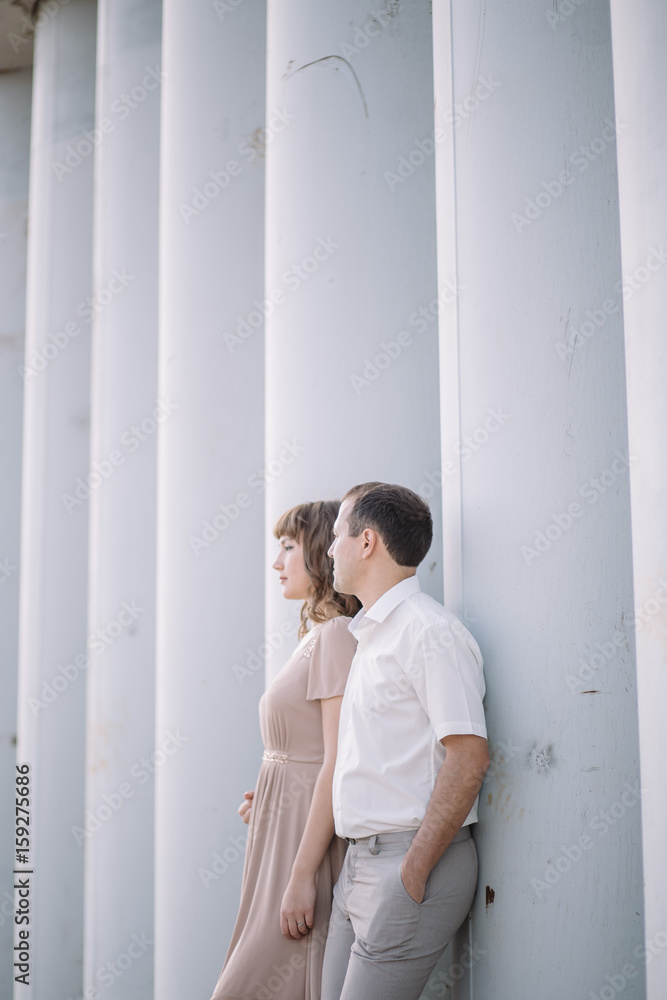 a love story, a man and a woman wearing light clothes, standing near a grey wall, profile, hug, family, a date, a walk