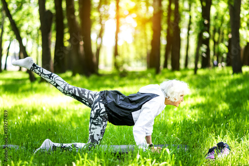 Concentrated old woman training yoga exercises in park