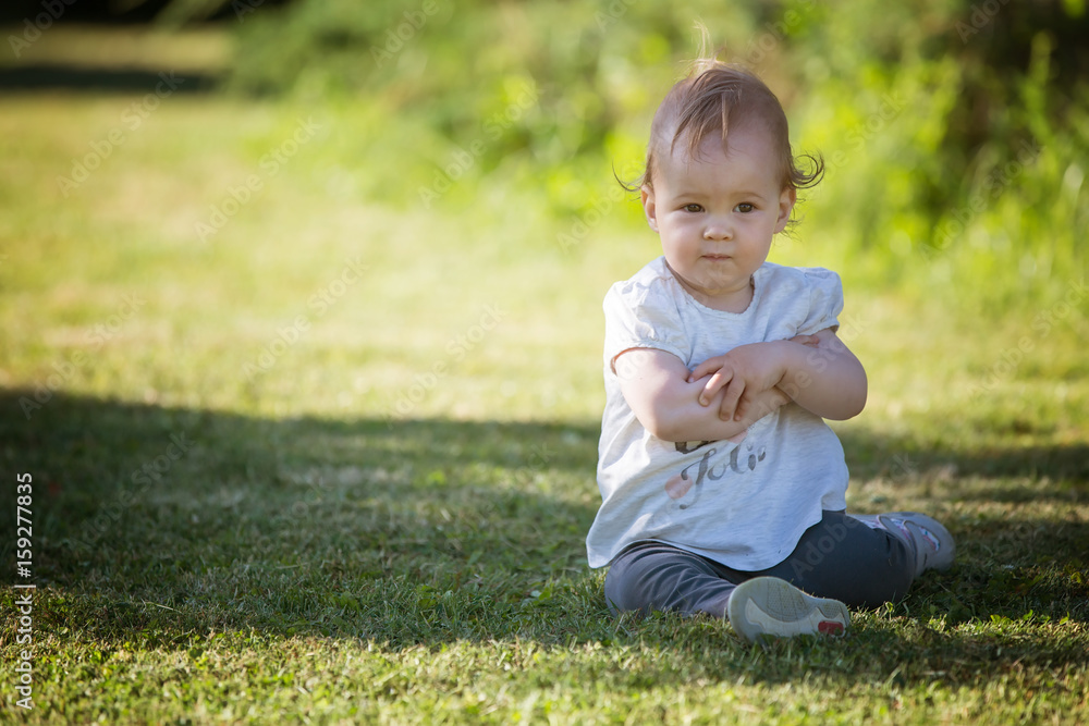 Fourteen months old baby girl sitting in the shadow on the grass on the sunny summer day Fourteen months old baby girl sitting in the shadow on the grass on the sunny summer day
