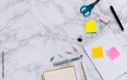 Creative mock-up flat lay of stationery on white marble texture background - Work space concept compose of notebook, post-it, pen, pencil, rubber, clip, scissors, calculator, and stapler