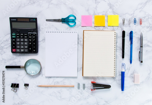 Creative mock-up flat lay of stationery on white marble texture background - Work space concept compose of notebook, post-it, pen, pencil, rubber, clip, scissors, calculator, and stapler
