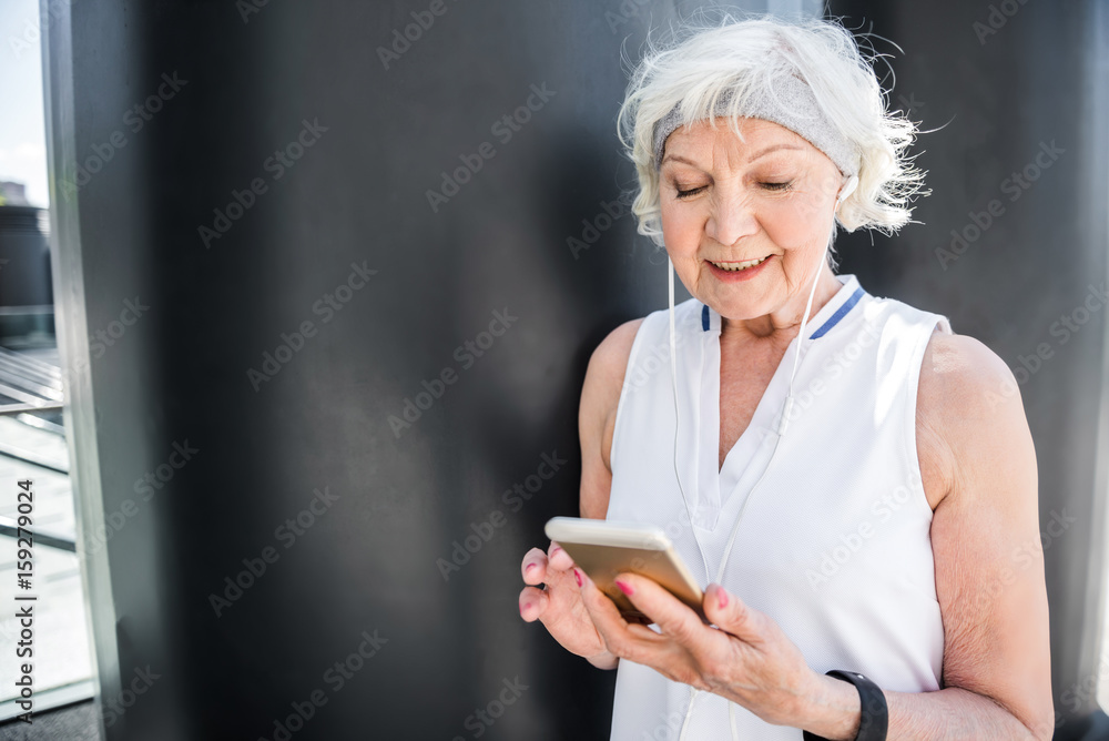 Cheery elderly lady texting through mobile phone outdoor