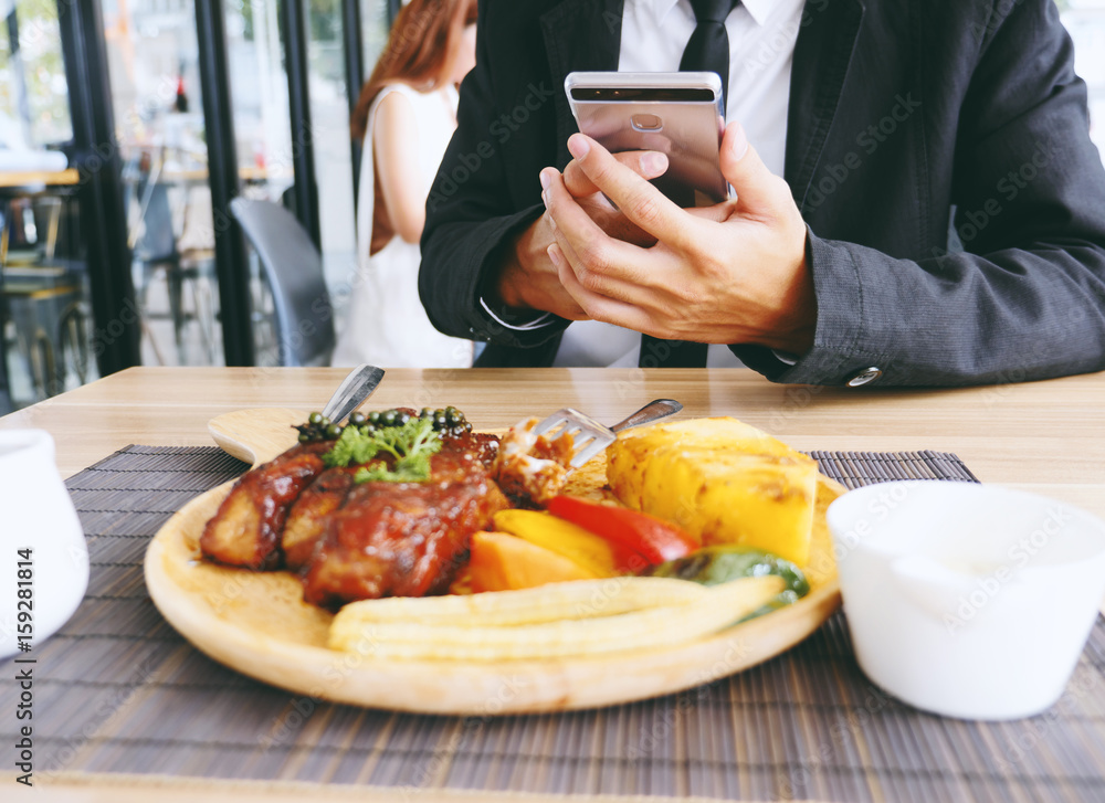 Businessman hand using smartphone to take photo of rib steak on wooden tray at restaurant.