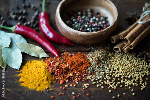 close up of pepper in bowl with scattered spices, laurel leaves, chili peppers on wooden tabletop photo