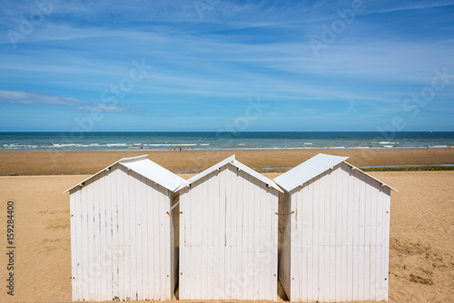 Three traditional white wooden beach huts on the beach of Villers, Normandy, France © Delphotostock