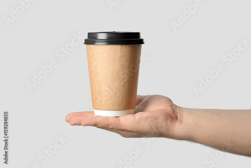 Mockup of male hand holding a Coffee paper cup isolated on light grey background. 