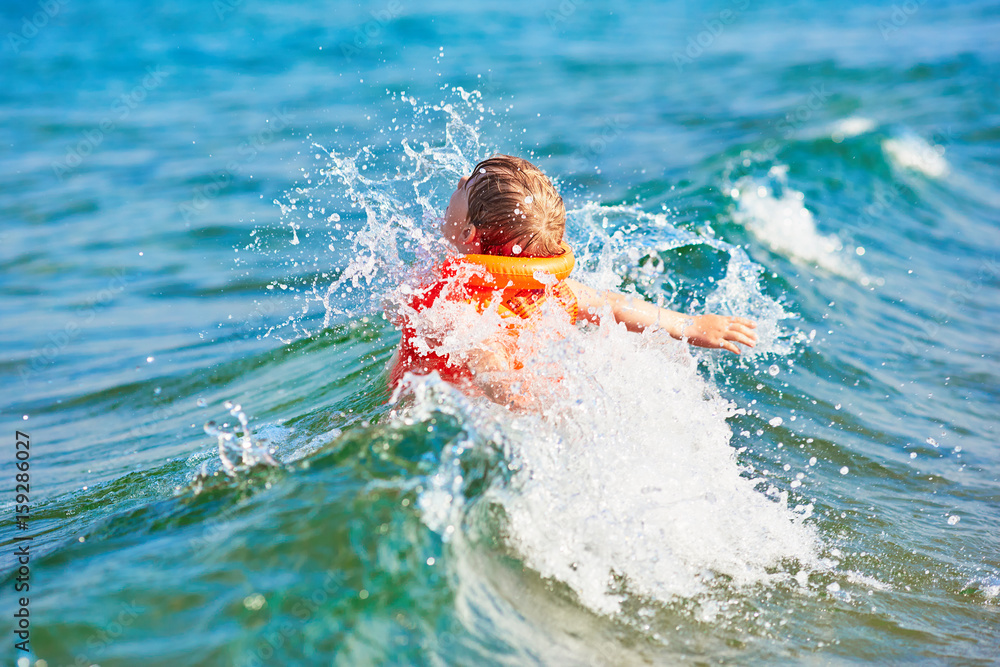Little boy in orange life vest swimming in wave sea (selective DOF)