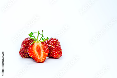 Two whole ripe strawberry berries and a cut berry in the foreground.