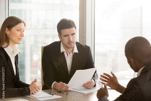 Black businessman trying to convince white doubtful partners to sign document, negotiations about contract, discussing deal, afro american job applicant persuades employers to hire, tell arguments