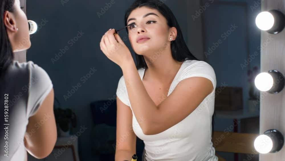 Beautiful woman tint eyelashes looking in the mirror. Doing eye make-up. Beautiful woman tint eyelashes looking in the mirror. Doing eye make-up.