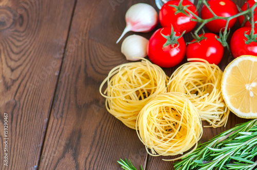 Raw ingredients for italian style dinner. Pasta, cherry tomatoes, garlic, rosemary on a wooden table. Close up and copy space.
