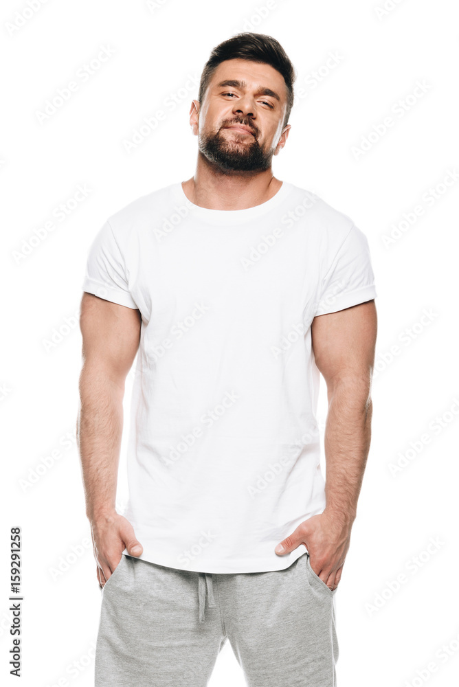 Portrait of muscular bearded man standing with hands in pockets and looking at camera isolated on white Portrait of muscular bearded man standing with hands in pockets and looking at camera isolated on white