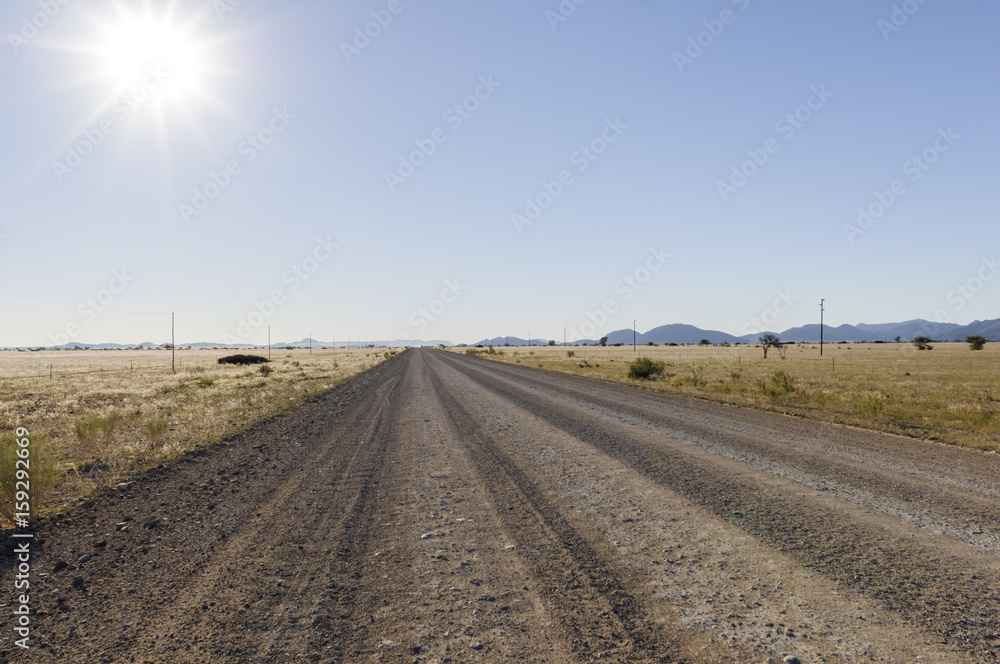 Landschaft mit gerader Strasse und Sonne / Landschaft mit gerader Strasse bis zum Horizont und Sonne, Namibia, Afrika.
