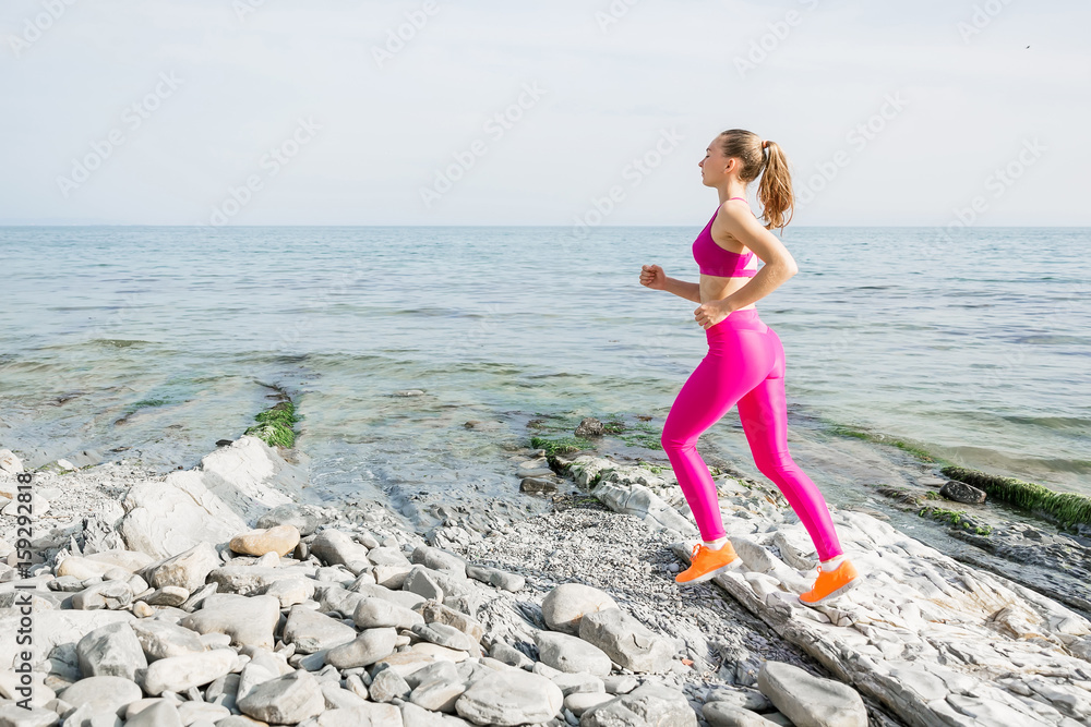 Slim fitness girl running on a beach. Woman with perfect body